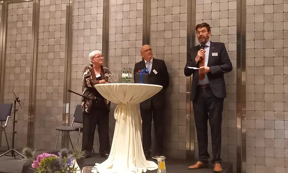 Drei Redner auf einer Bühne.